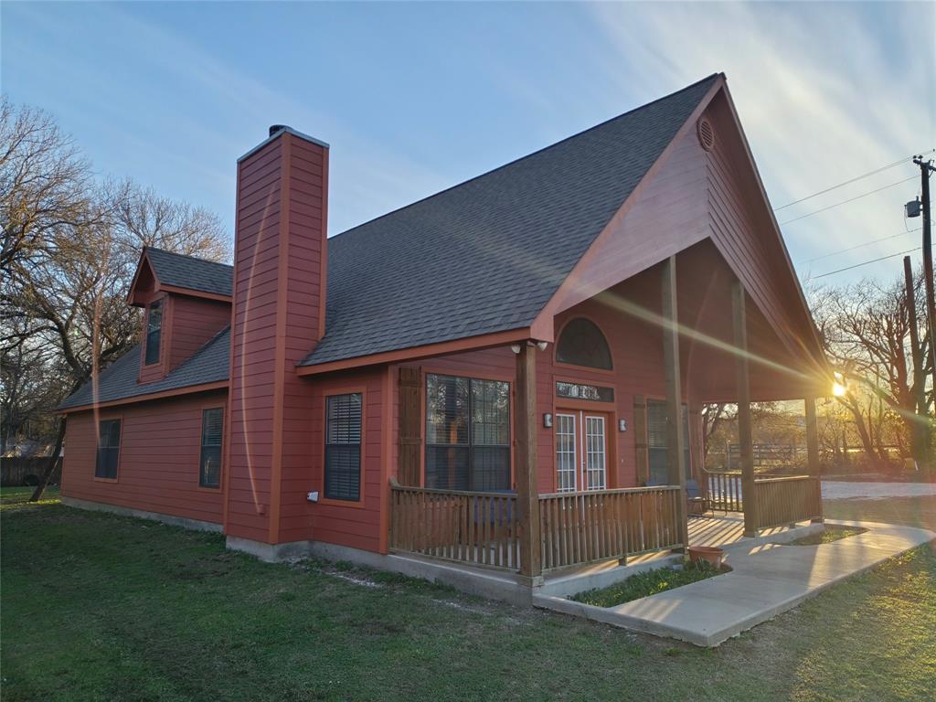 Back of property featuring a shingled roof, a porch, a chimney, and a lawn