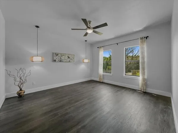 an empty room with wooden floor chandelier fan and windows