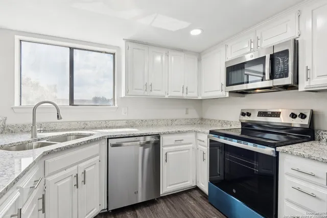 a kitchen with stainless steel appliances granite countertop white cabinets a sink and a stove