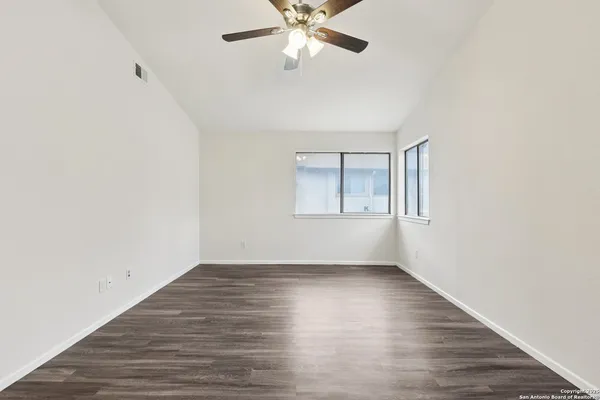 an empty room with wooden floor chandelier fan and windows