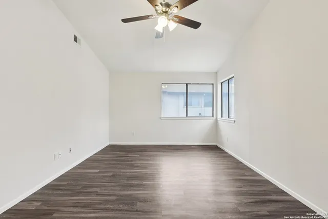 an empty room with wooden floor chandelier fan and windows