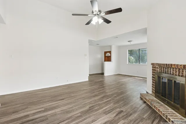 a view of an empty room with wooden floor ceiling fan