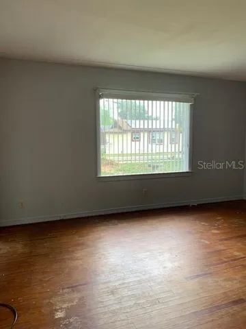 a view of an empty room with wooden floor and a window