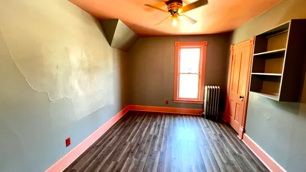 a view of empty room with wooden floor and fan