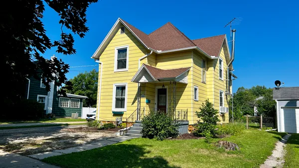 a view of a house with a small yard and a large tree