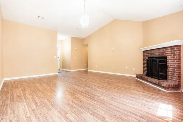 a view of an empty room with wooden floor fireplace and a window