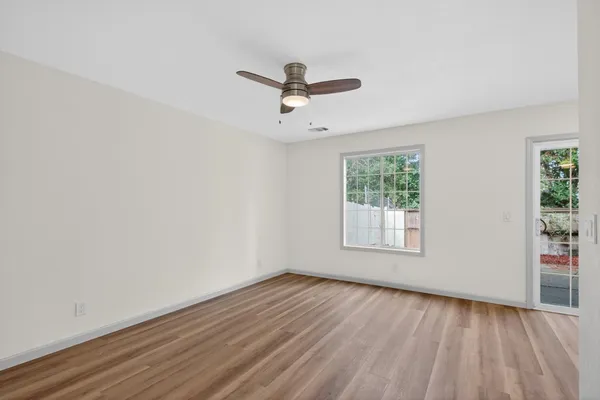 an empty room with wooden floor ceiling fan and windows