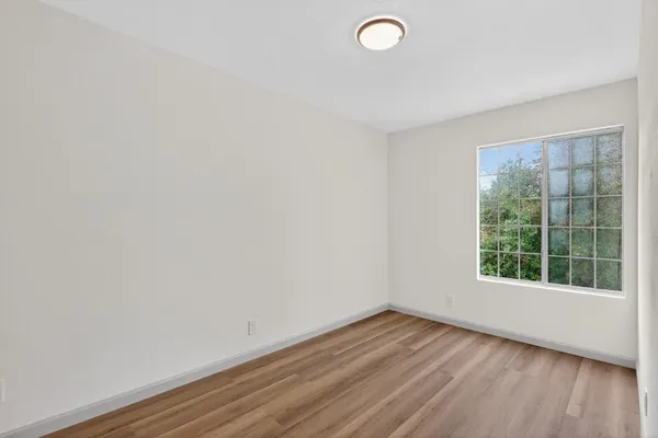 a view of an empty room with wooden floor and a window