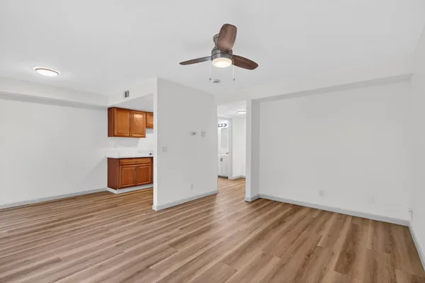 a view of an empty room with wooden floor and a ceiling fan