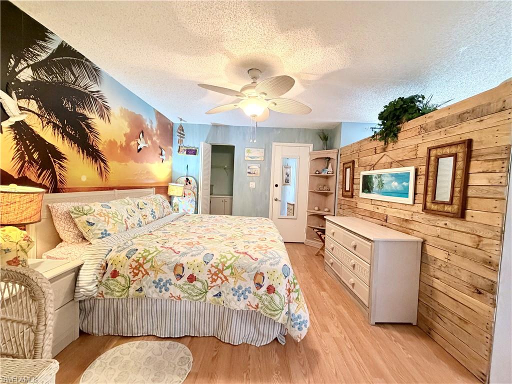 5800 Bonita Beach Road Southwest, Unit 2805 Bonita Springs, FL 34134 - Photo 13 of 30 Bedroom featuring wood walls, a textured ceiling, light wood finished floors, and ceiling fan