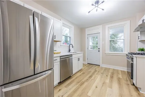 a kitchen with stainless steel appliances a sink cabinets wooden floor and a window