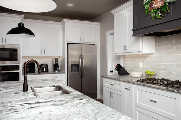 a kitchen with stainless steel appliances kitchen island granite countertop a refrigerator a stove a sink and white cabinets with wooden floor