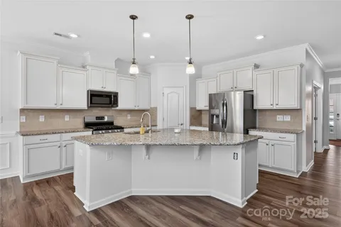 a kitchen with stainless steel appliances granite countertop a sink a stove a refrigerator and white cabinets with wooden floor