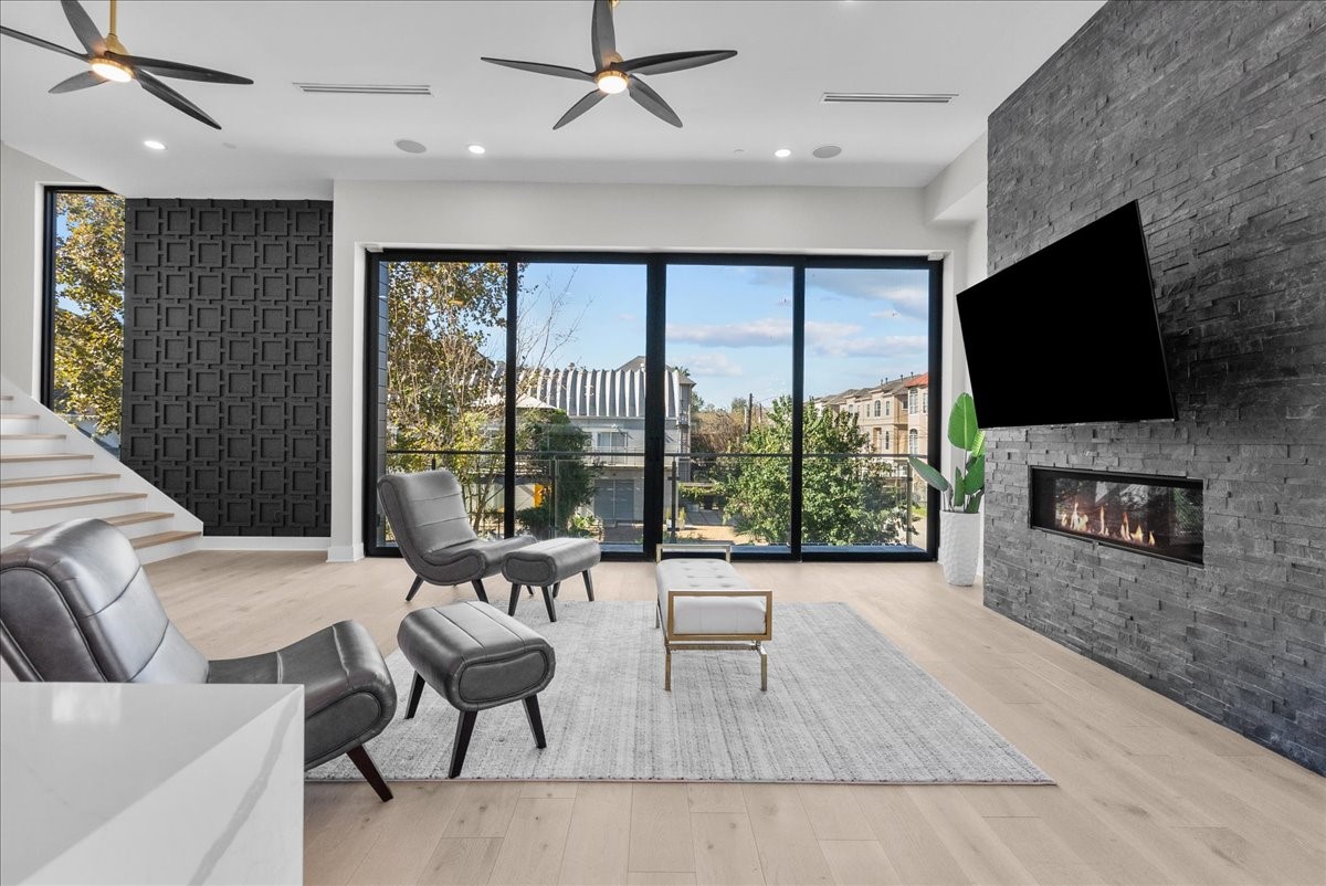 516 Reinerman Street Houston, TX 77007 - Photo 22 of 42 This modern living room features large floor-to-ceiling windows with a scenic view, a sleek black accent wall, and a cozy fireplace. The space is airy and bright, with stylish furnishings and contemporary ceiling fans, creating a perfect blend of comfort and elegance.