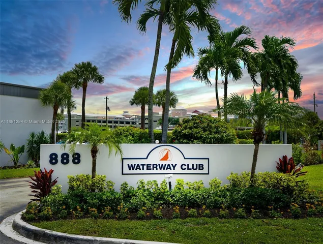 a sign that is sitting on the grass and palm tree