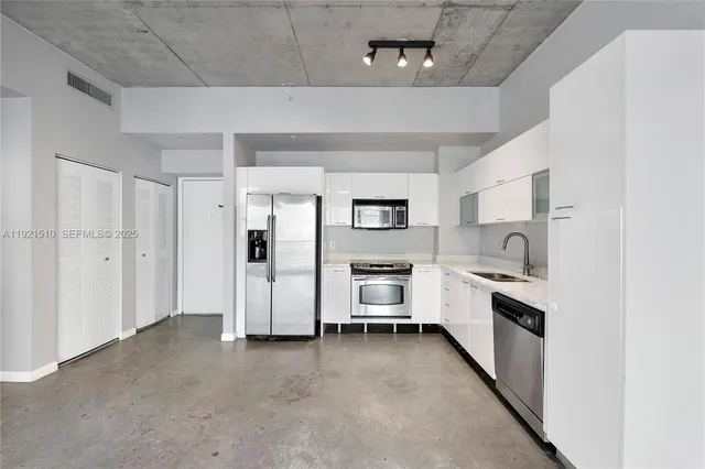 a kitchen with stainless steel appliances a refrigerator a sink a stove and white cabinets