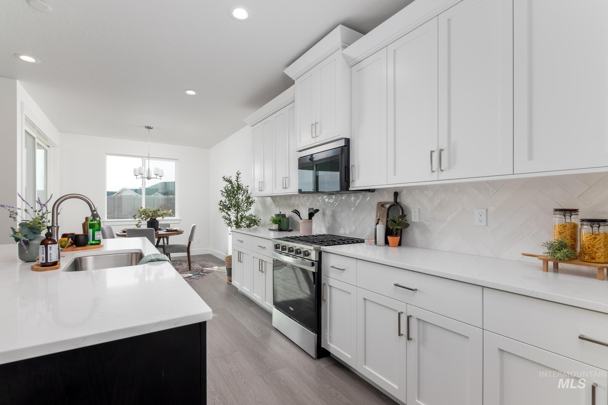 1761 West Arya Street Kuna, ID 83634 - Photo 6 of 12 Kitchen featuring stainless steel appliances, light stone countertops, white cabinets, light wood-style floors, and backsplash