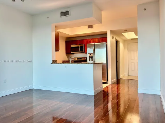 a view of a hallway with wooden floor and a kitchen