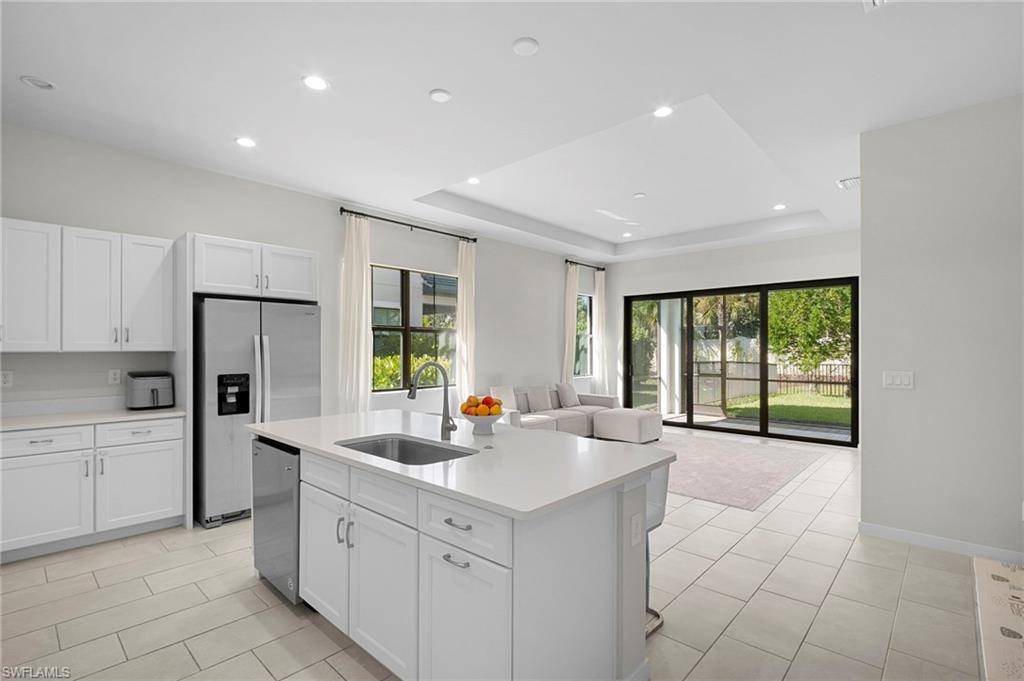 14720 Kingfisher Loop Naples, FL 34120 - Photo 49 of 50 Kitchen featuring stainless steel appliances, open floor plan, a center island with sink, white cabinets, and plenty of natural light