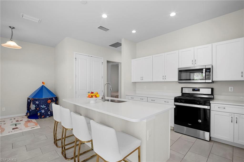 14720 Kingfisher Loop Naples, FL 34120 - Photo 6 of 50 Kitchen with stainless steel appliances, a center island with sink, white cabinetry, a kitchen bar, and hanging light fixtures