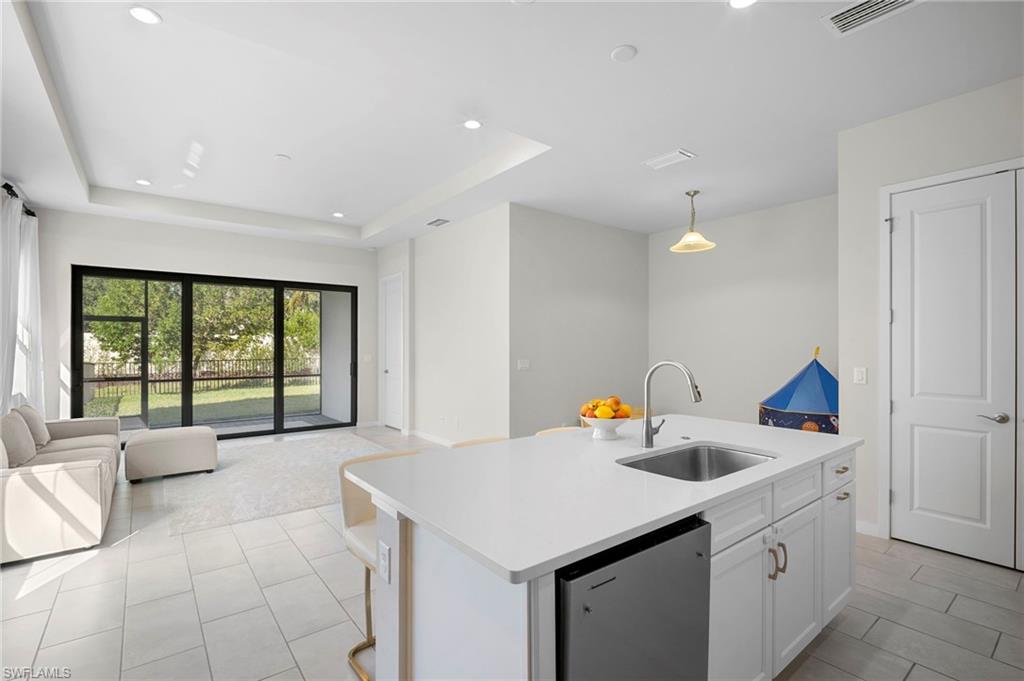 14720 Kingfisher Loop Naples, FL 34120 - Photo 50 of 50 Kitchen featuring open floor plan, a center island with sink, stainless steel dishwasher, a tray ceiling, and white cabinetry