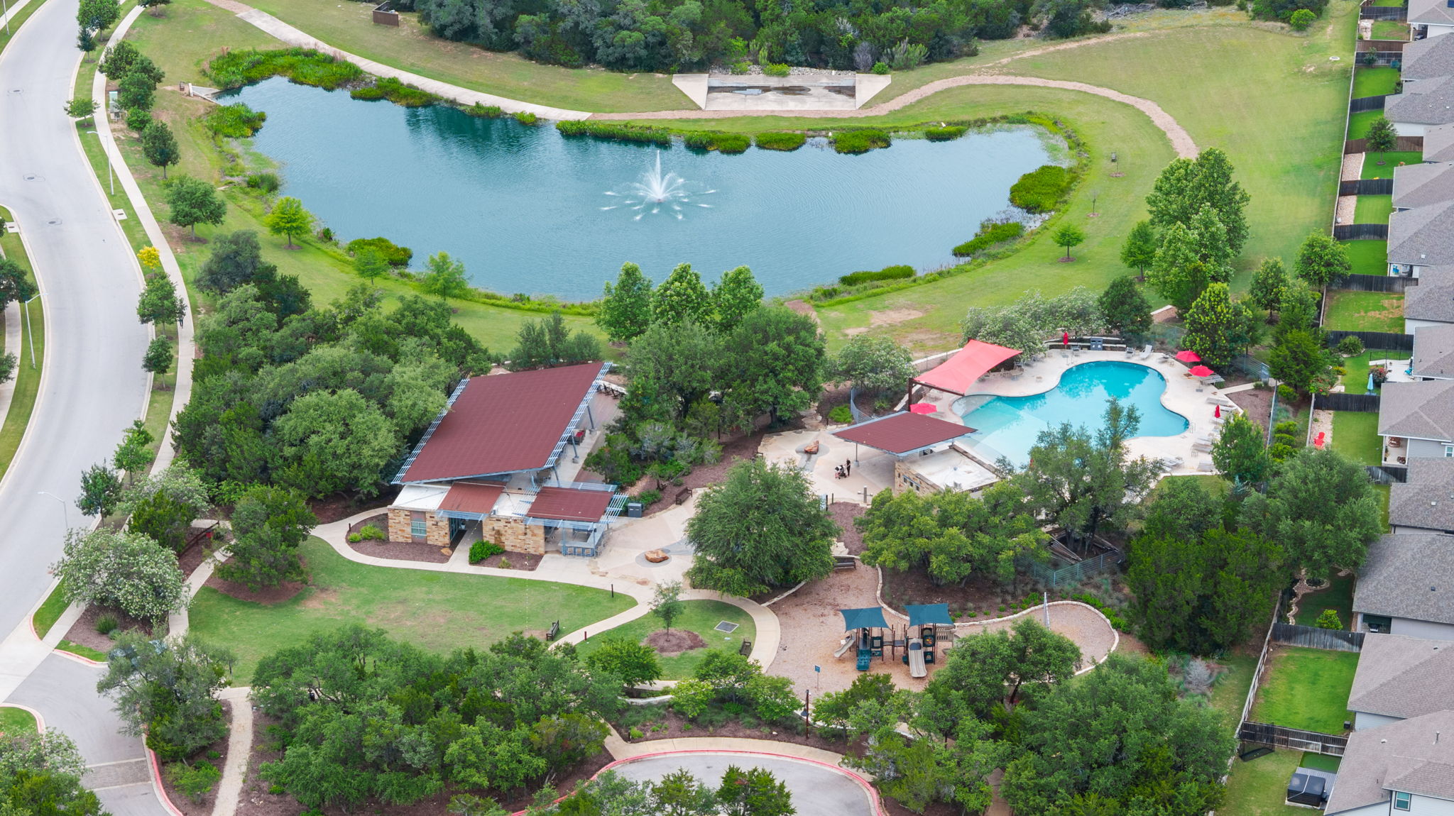 1908 Woolsey Way Leander, TX 78641 - Photo 31 of 36 An aerial view highlights the community/ amenity center & refreshing pool, nearby playground, and serene pond with a fountain feature.