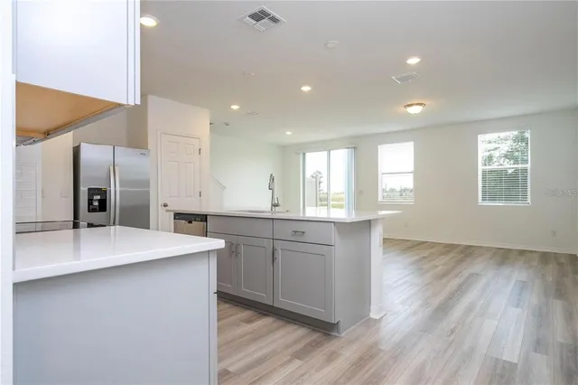 a large kitchen with kitchen island a sink dishwasher a refrigerator and white cabinets with wooden floor