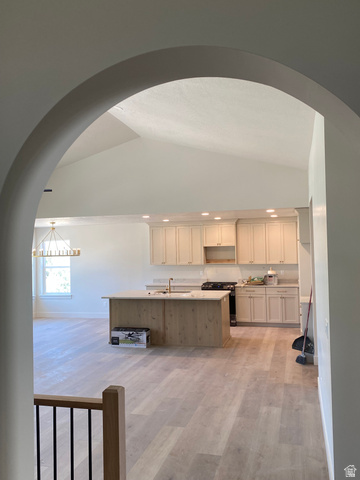 4676 West 75 North, Unit 401 West Point, UT 84015 - Photo 13 of 25 Arched entryway framing a kitchen with light wood-finish flooring, recessed lighting, a central island with a sink, and light-toned cabinetry