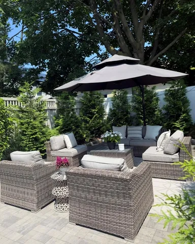 a view of a patio with couches table and chairs under an umbrella with large trees