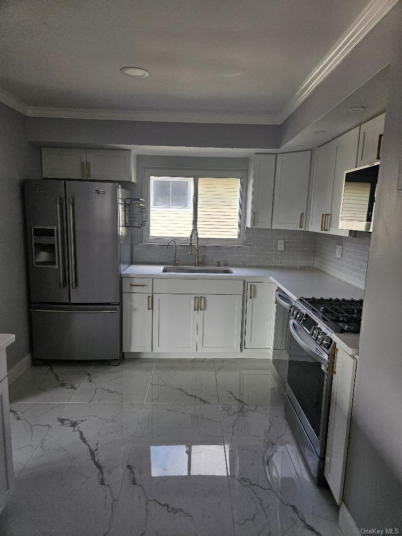 149 Truxton Road Dix Hills, NY 11746 - Photo 11 of 22 Kitchen with crown molding, white cabinets, light marble finish floors, appliances with stainless steel finishes, and decorative backsplash