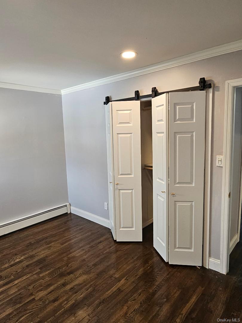 149 Truxton Road Dix Hills, NY 11746 - Photo 16 of 22 Unfurnished bedroom with a barn door, ornamental molding, baseboard heating, dark wood-type flooring, and a closet