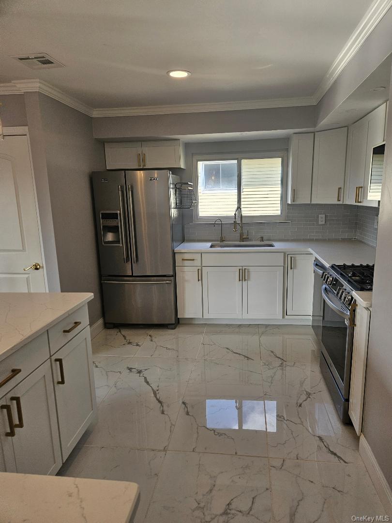 149 Truxton Road Dix Hills, NY 11746 - Photo 9 of 22 Kitchen with stainless steel appliances, white cabinets, ornamental molding, light marble finish floors, and light stone countertops