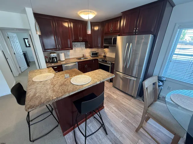 a kitchen with stainless steel appliances granite countertop a refrigerator a stove a sink dishwasher and wooden cabinets with wooden floor