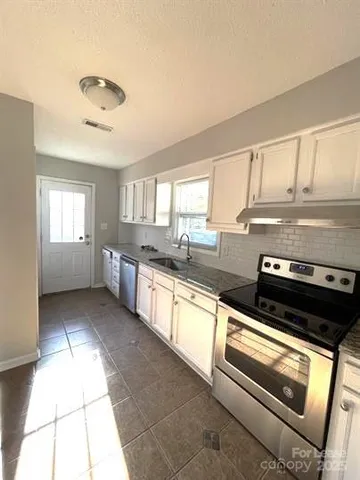 a kitchen with stainless steel appliances granite countertop a stove a sink and white cabinets