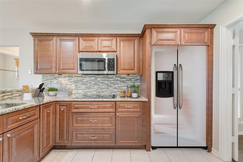 11374 Jennifer Circle Forney, TX 75126 - Photo 14 of 36 Kitchen featuring stainless steel appliances, light stone counters, wood finish cabinetry, and tasteful backsplash.