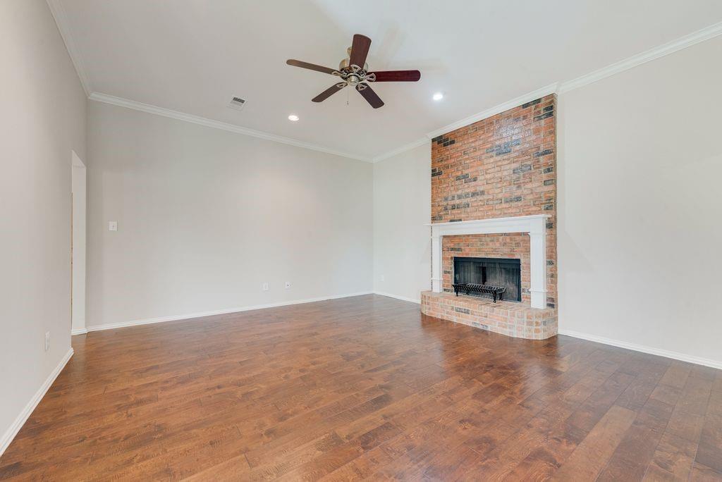 11374 Jennifer Circle Forney, TX 75126 - Photo 9 of 36 Unfurnished living room featuring dark wood-style flooring, a ceiling fan, crown molding, a brick fireplace, and recessed lighting.