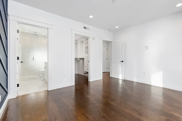 a view of an empty room with wooden floor and a bathroom