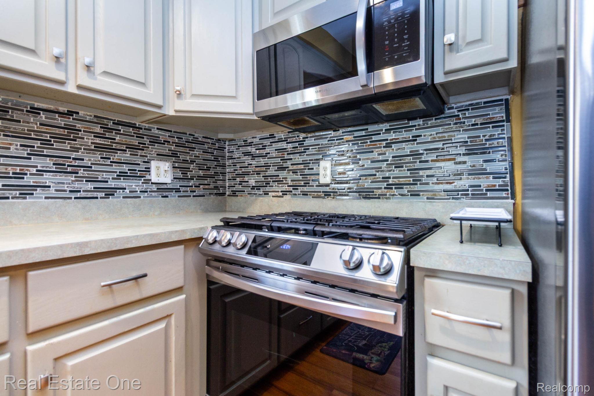 220 Winry Drive Rochester, MI 48307 - Photo 13 of 35 Modern kitchen featuring stainless steel appliances, light-toned cabinetry, a mosaic tile backsplash, and light-colored countertops