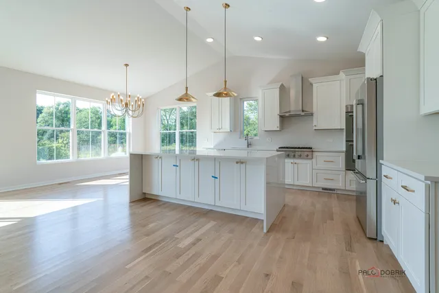 a kitchen with stainless steel appliances granite countertop a refrigerator a sink dishwasher a stove and white cabinets with wooden floor