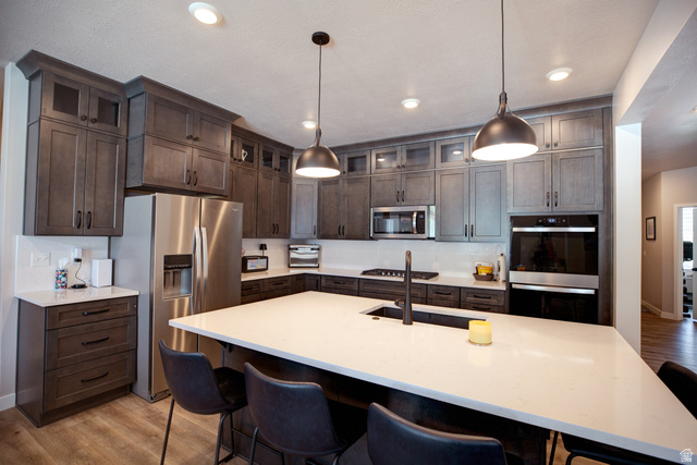 983 South 950 West Provo, UT 84601 - Photo 12 of 56 Modern kitchen featuring dark wood-finish cabinetry, stainless steel appliances, a white countertop island with seating, and pendant lighting