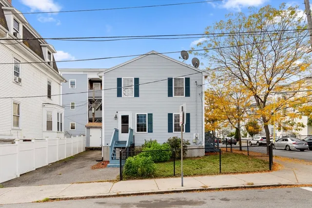 a view of a white house with large tree and wooden fence