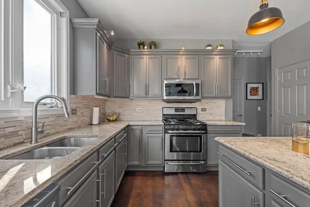 a kitchen with stainless steel appliances granite countertop a stove top oven a sink a dining table and chairs with wooden floor