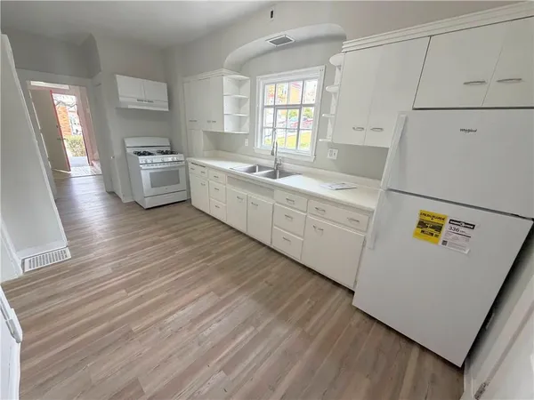 a large kitchen with a stove a refrigerator a sink dishwasher and white cabinets with wooden floor