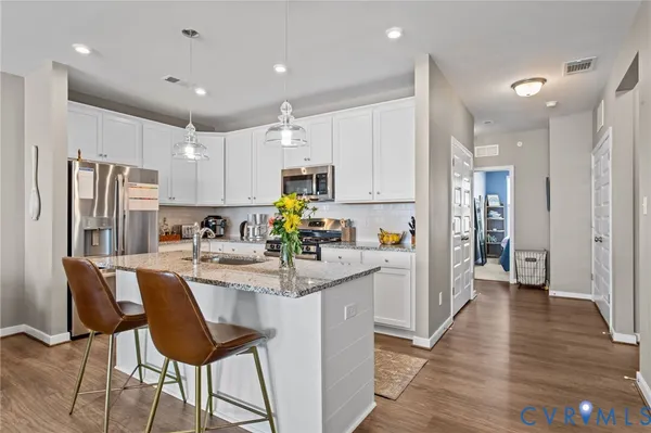 a kitchen with stainless steel appliances granite countertop a refrigerator a sink dishwasher a stove and white cabinets with wooden floor