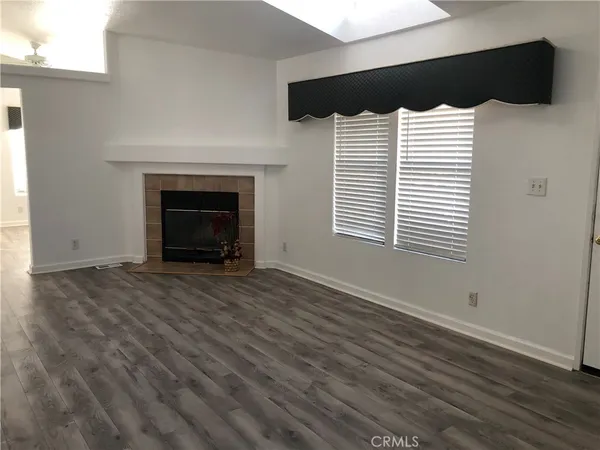 a view of an empty room with wooden floor fireplace and a window