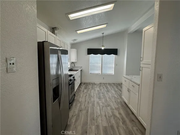 a kitchen with stainless steel appliances kitchen island granite countertop a stove top oven a sink a refrigerator white cabinets and wooden floor