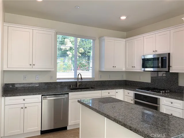 a kitchen with granite countertop white cabinets sink and stainless steel appliances