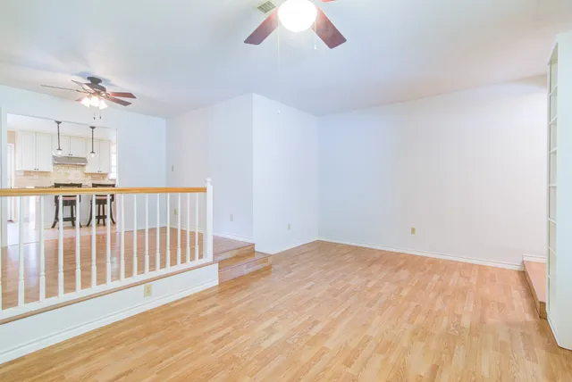an empty room with wooden floor windows and a chandelier fan
