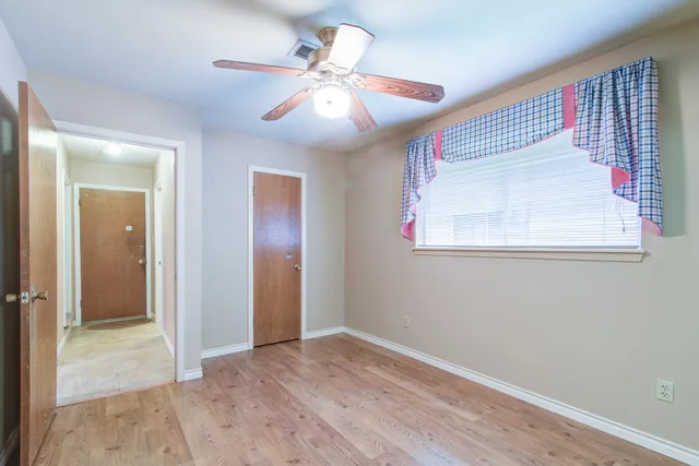 an empty room with wooden floor fan and windows