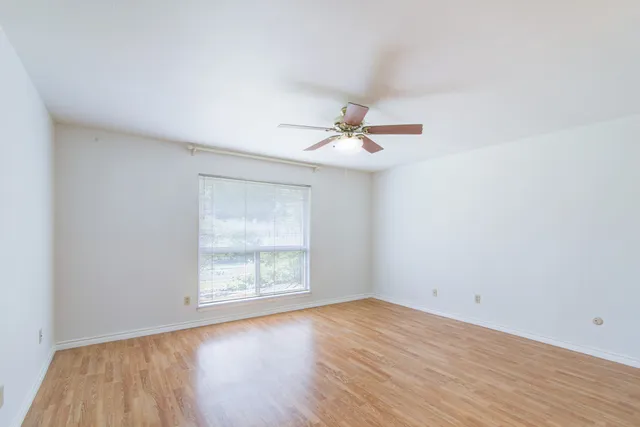 an empty room with wooden floor fan and windows